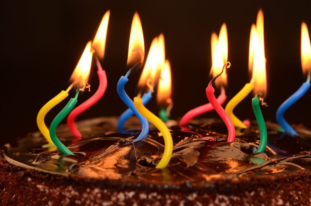 top of chocolate-iced cake with flaming, twisted birthday candles in primary colors