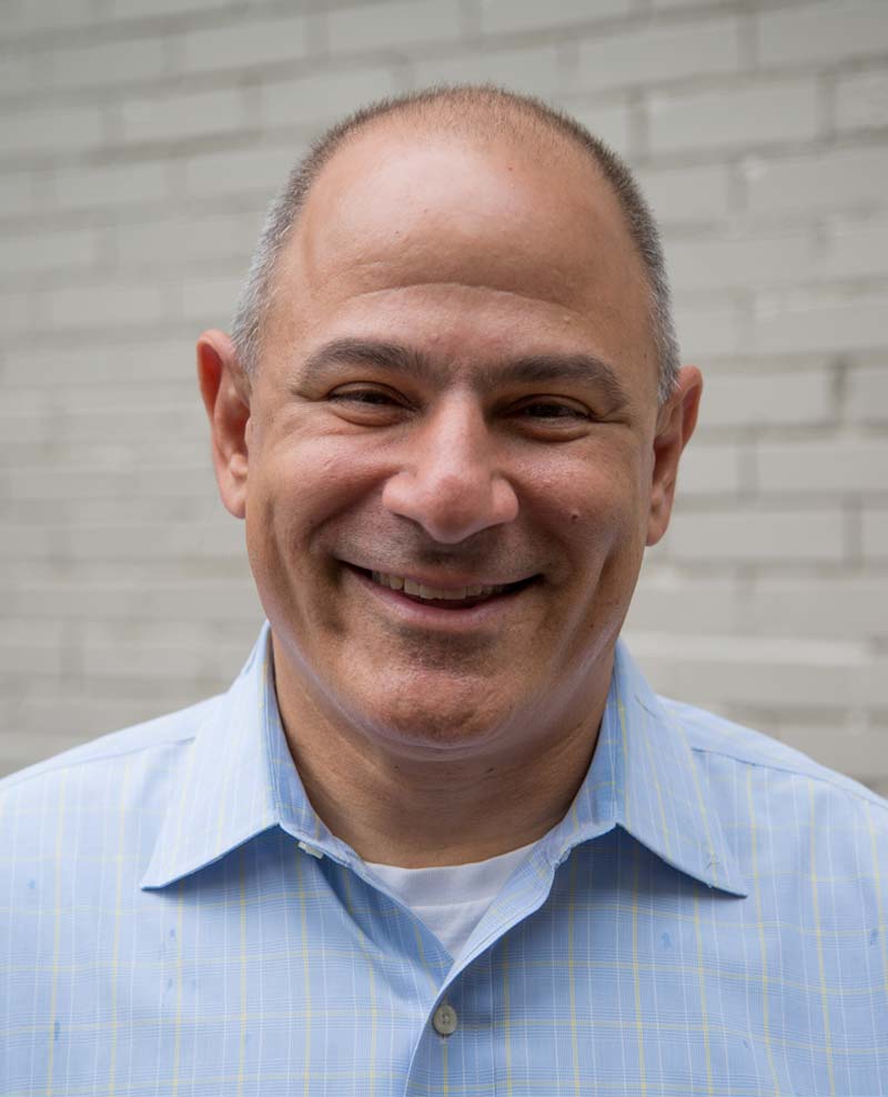 smiling white man with short salt-and-pepper hair wearing a light blue shirt open at the neck