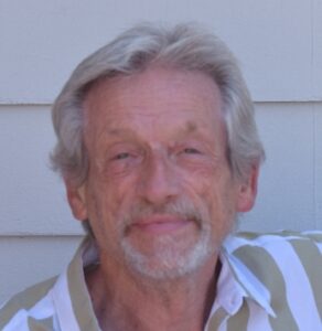 white man with grey hair, beard, and mustache in tan-and-white striped shirt