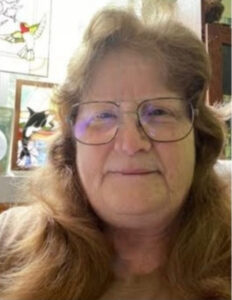 White woman with long, wavy brown hair wearing thin-rimmed glasses.